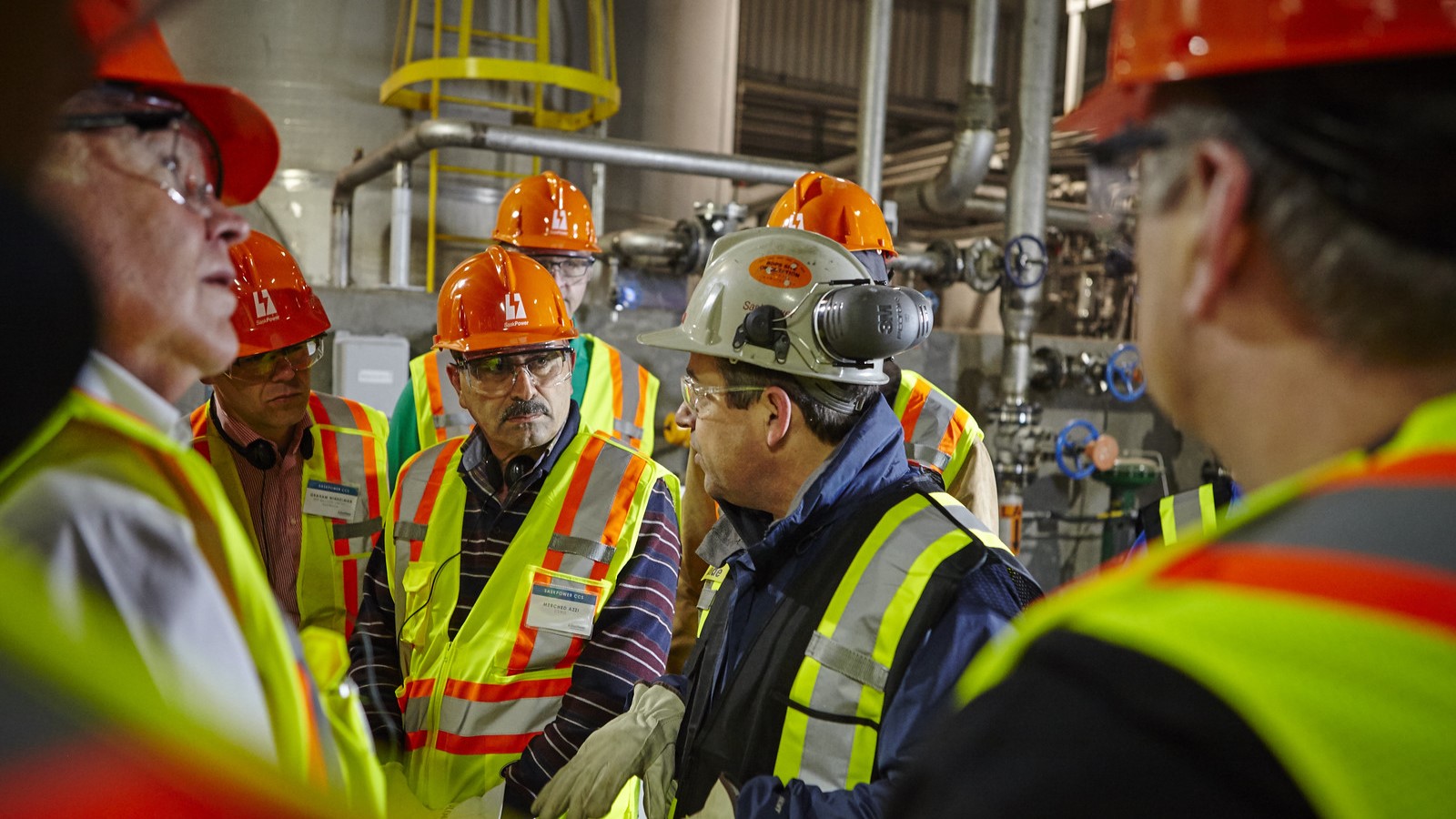 Men in safety vests and hard hats huddled together at a carbon capture facility.
